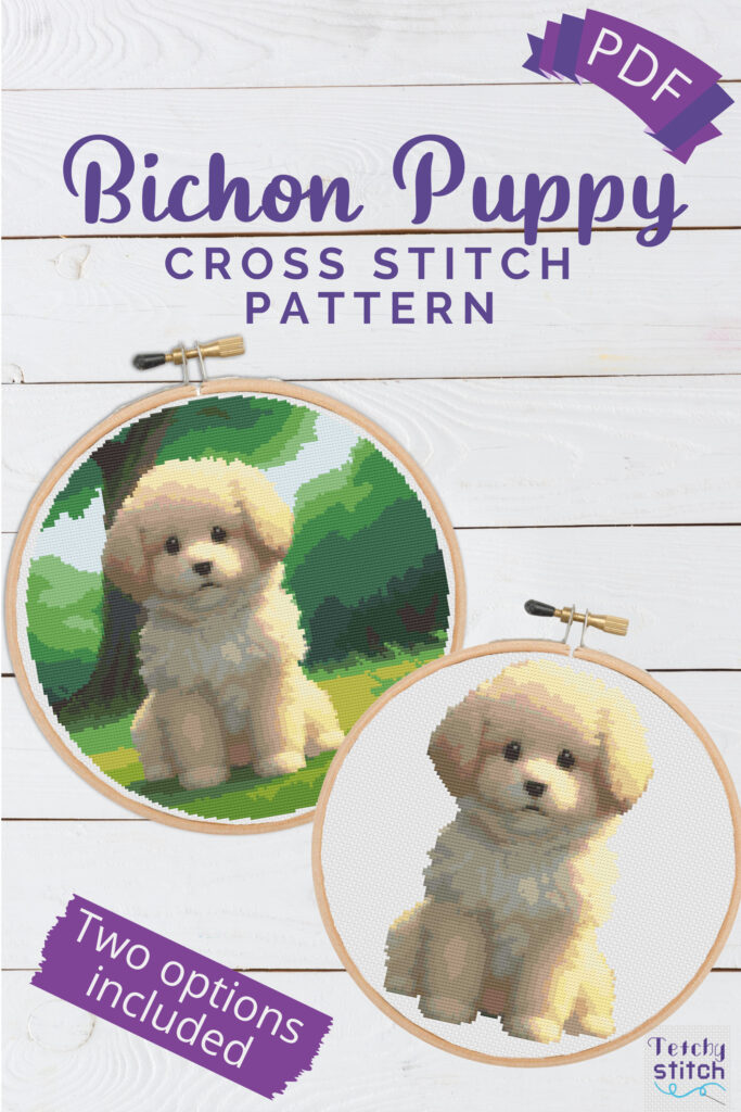 Two bichon frise puppy cross stitch designs in embroidery hoops lying on a white wood table
