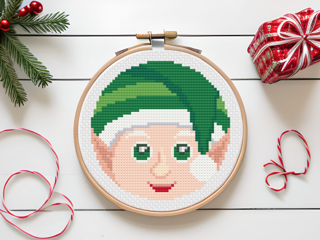 Christmas elf cross stitch pattern on white table with Christmas decorations