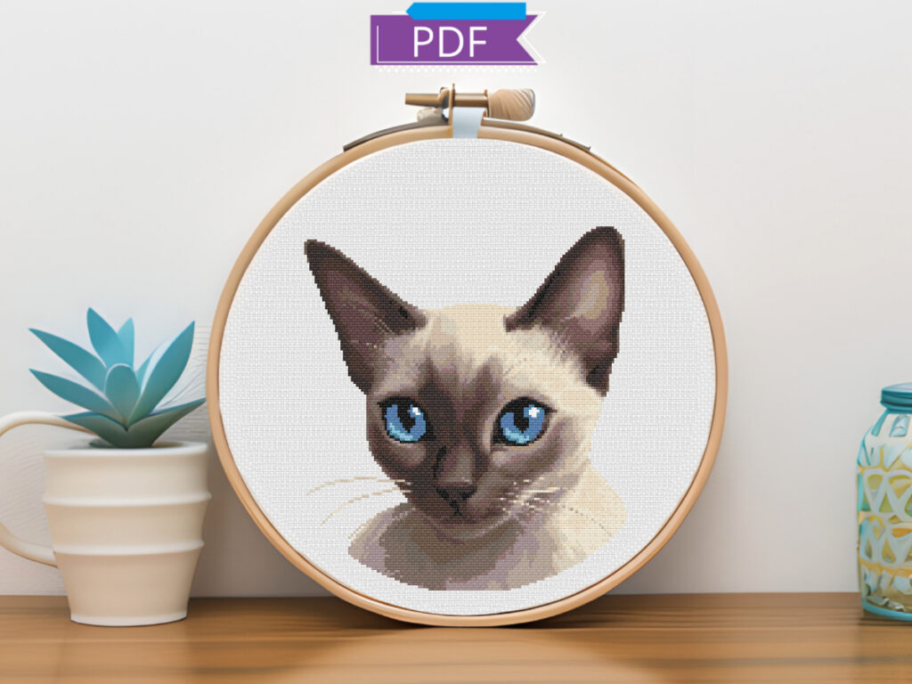 Siamese cat cross stitch in a hoop resting on a shelf