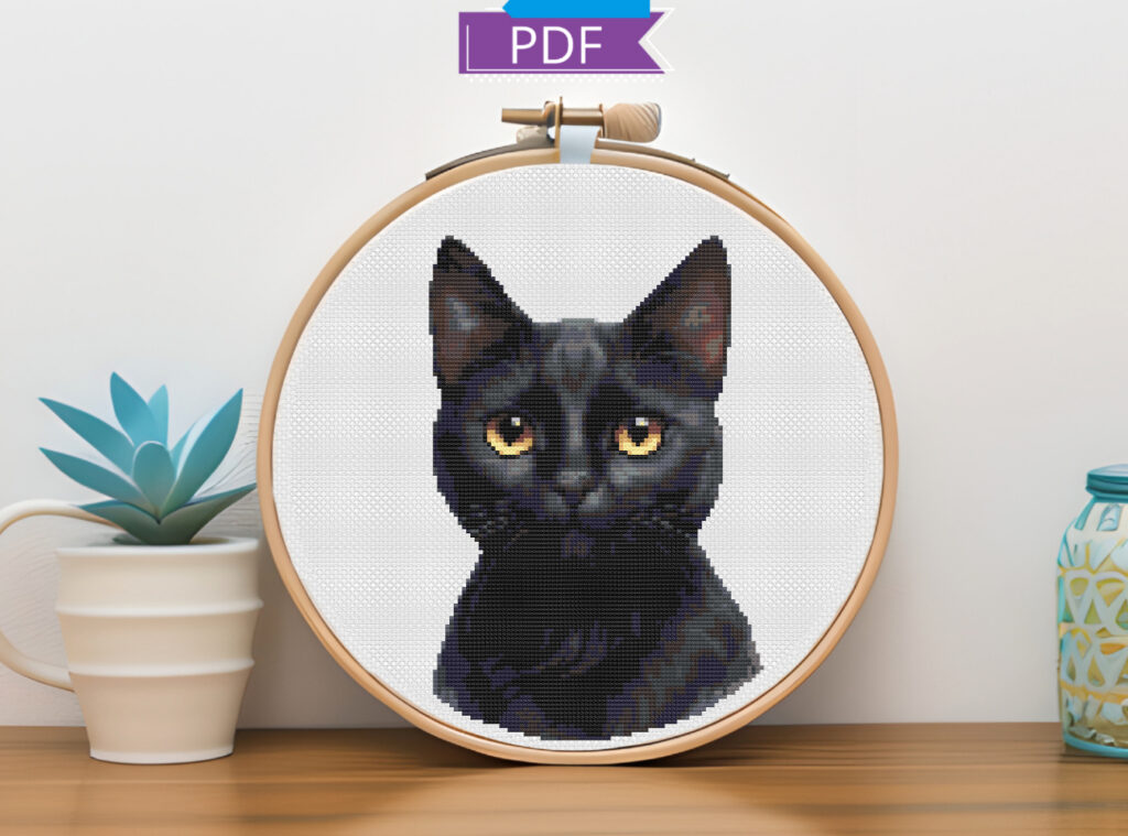 Black cat cross stitch pattern on white Aida cloth in a wooden embroidery hoop